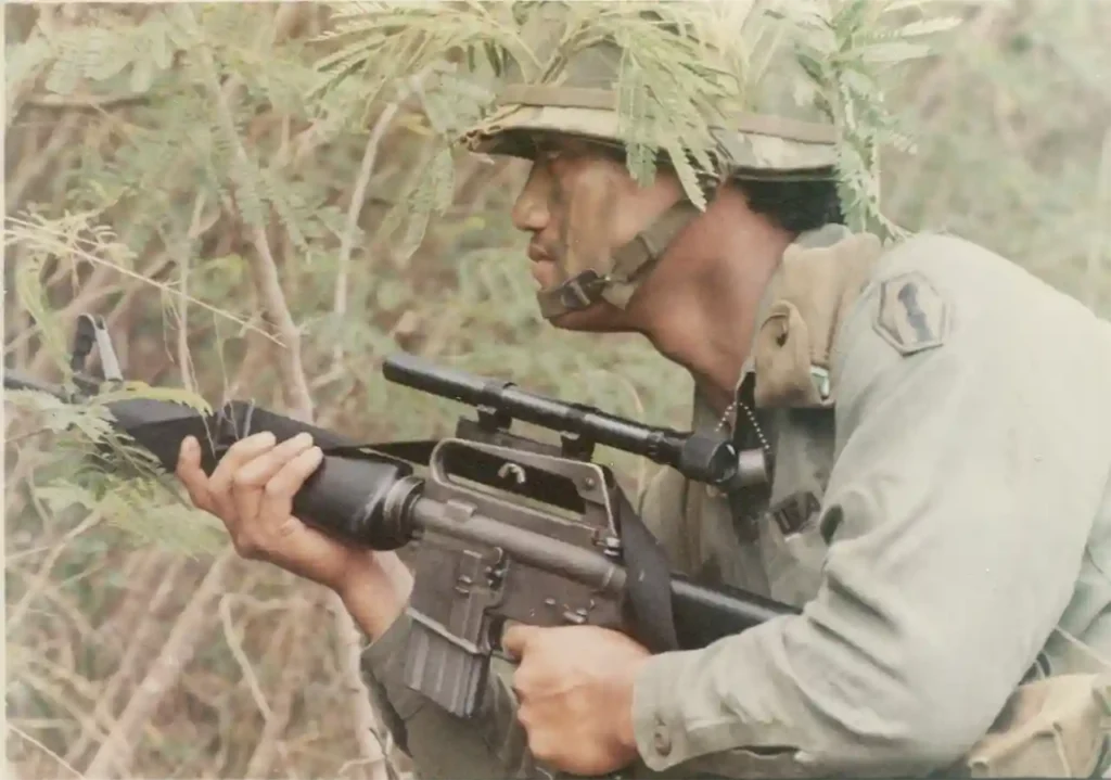 A reservist of the 100th Infantry Battalion, 442d Infantry, moves through a thicket with his M16 rifle equipped with a sniper scope during annual summer training in Makua Valley, Hawai’i, 10 August 1975. (National Archives)