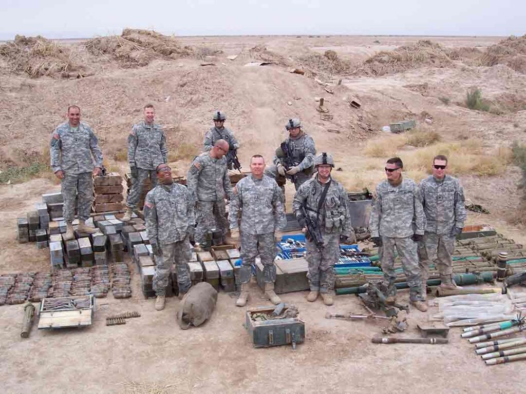 Troopers of 5-73 CAV stand before an insurgent weapons cache that includes small arms ammunition, rocket-propelled grenades, hand grenades, and an 82mm recoilless rifle. (Ray Edgar)