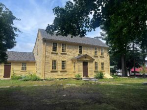 A two story yellow house with a front entrance in the middle of the first story with a brown door and small awning. There are five windows on the second story (the middle one is directly over the front door) and on the first floor there are two window on either side of the door.