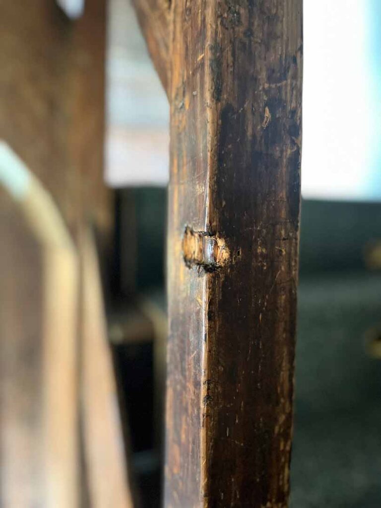 In the immediate foreground of the photograph is a vertical wooden beam that has a chunk of wood torn out of the front corner that was cause by a musket ball shot into the house.