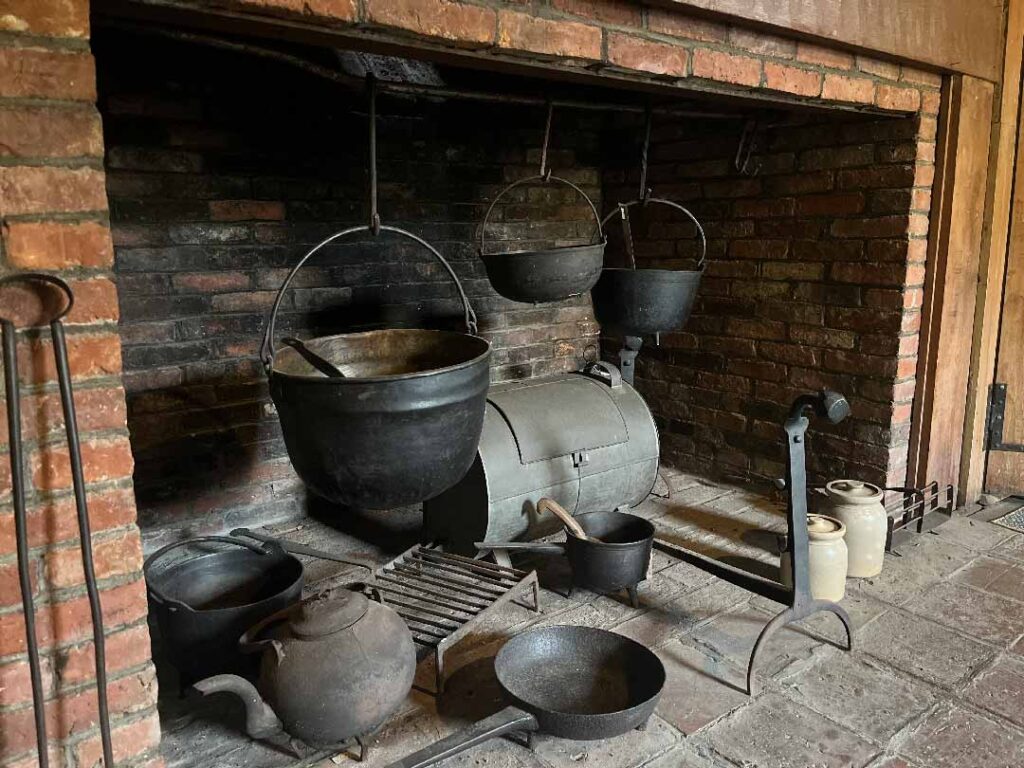 Large pots and pans hang from the top top of a brick hearth.