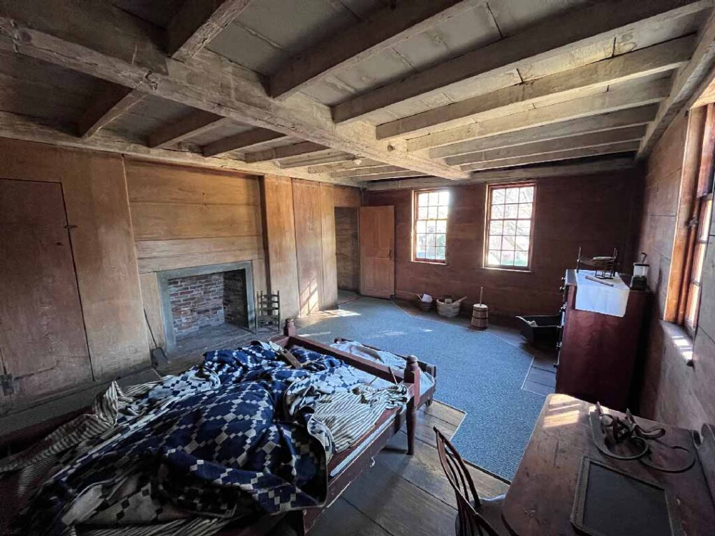 A bedroom with one bed with blue and white patterned covers, a grey carpet used for modern day visitors to ensure the organization protects the wooden floors,