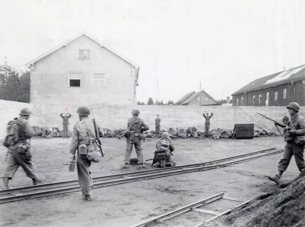 SS camp guards lined up in Dachau concentration camp’s coal yard, directly following a flurry of fire from American soldiers that killed approximately sixteen of the surrendered guards, 29 April 1945. Following the war, the reprisals committed at Dachau were investigated as war crimes, but the case was dropped without any charges due to the extenuating circumstances of the camp’s horrors. (National Archives) 