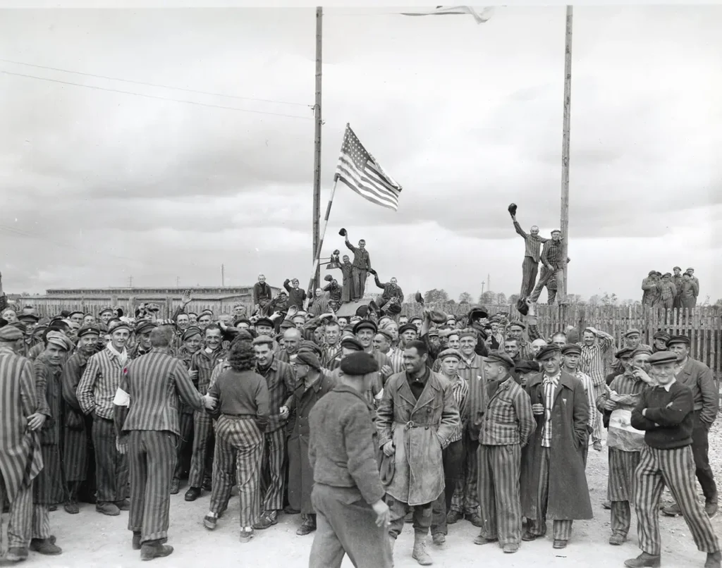 A homemade American flag crafted by inmates of the Dachau concentration camp is joyously waved by liberated prisoners, 29 April 1945. (National Archives) 